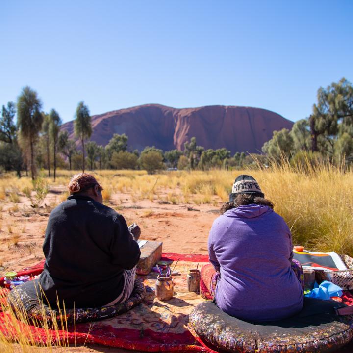 Two people sitting on blankets in front of Ayers Rock