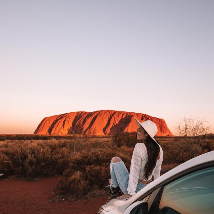 Woman sitting on car hood in front of Ayers Rock