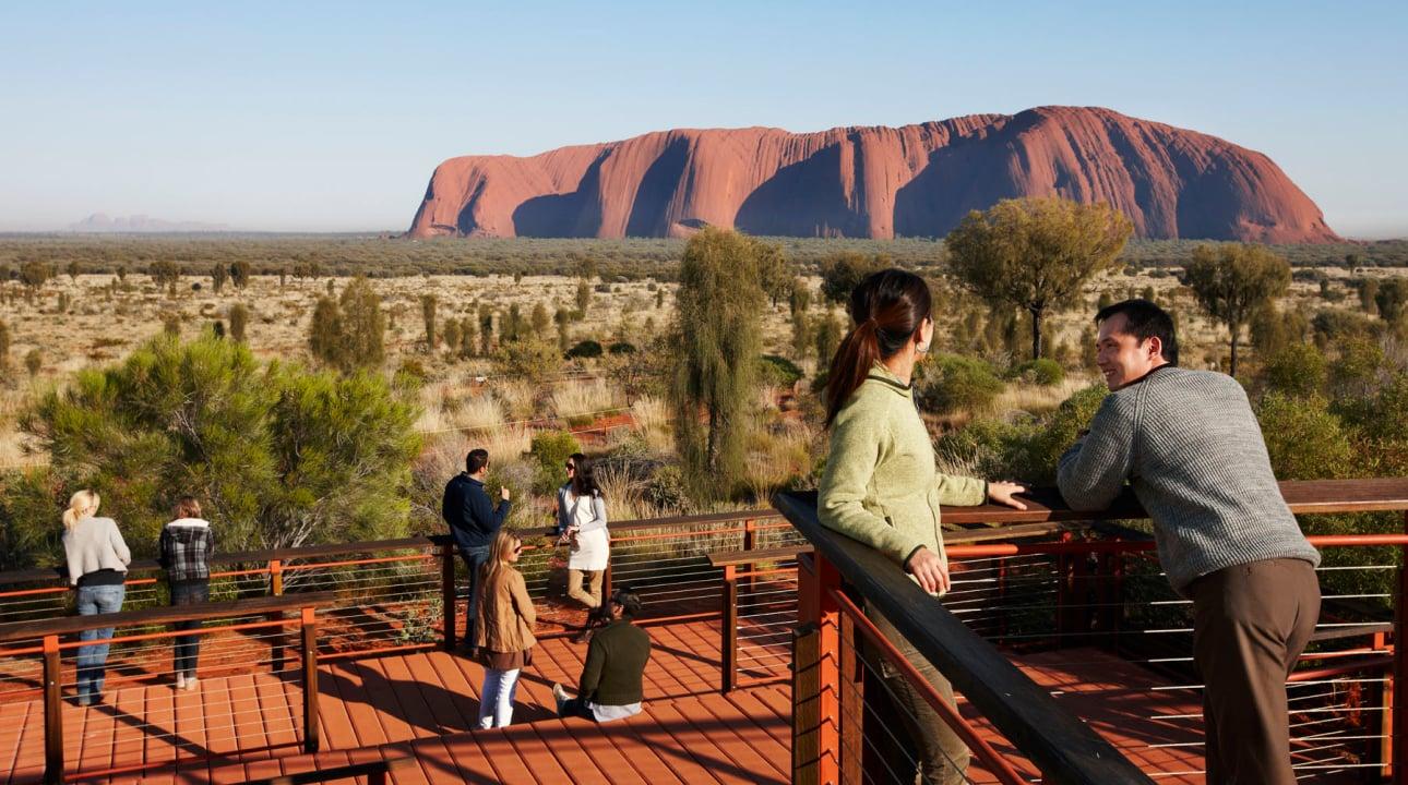 people on a deck with Ayers Rock in the background