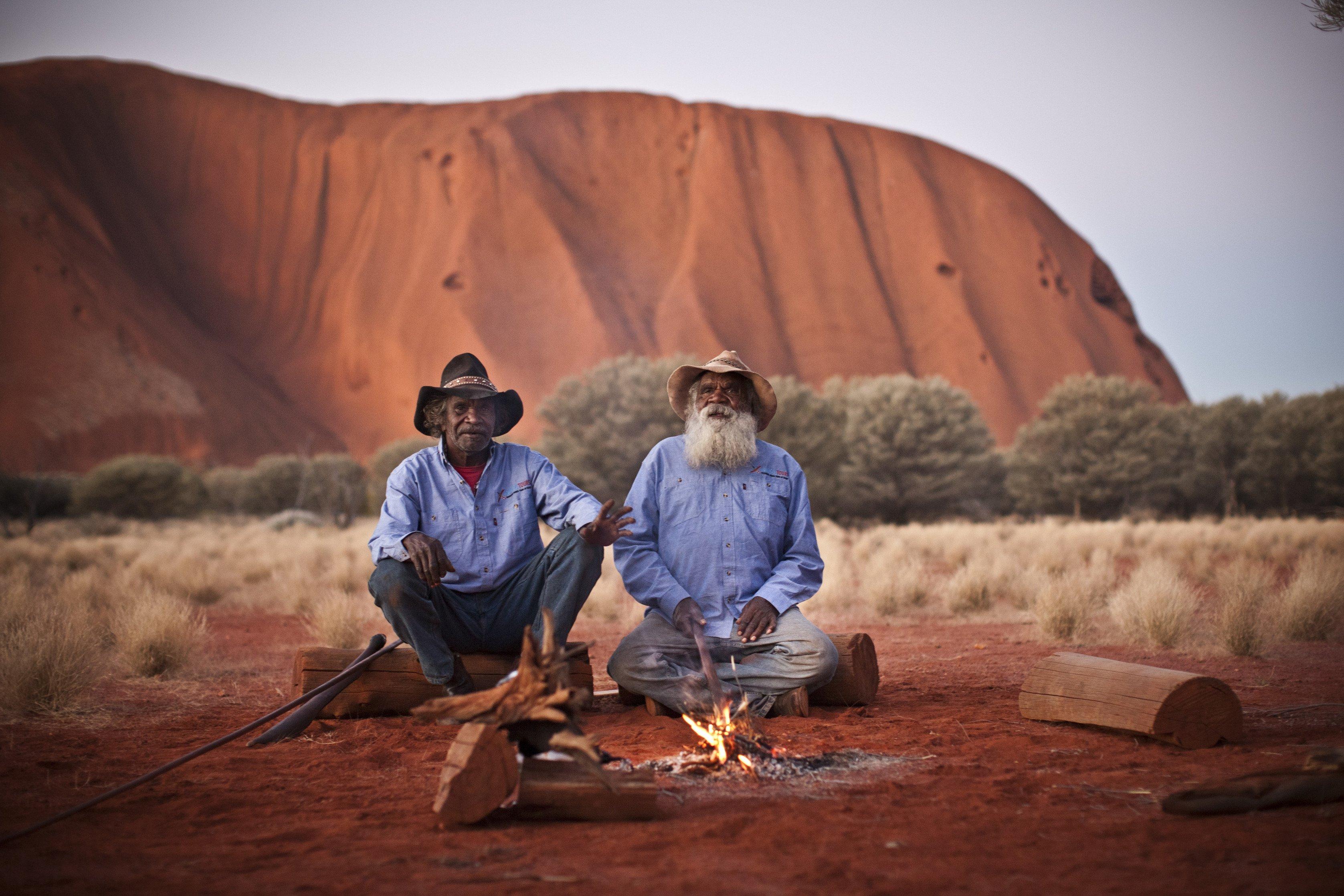 Two Anangu men sit by a fire