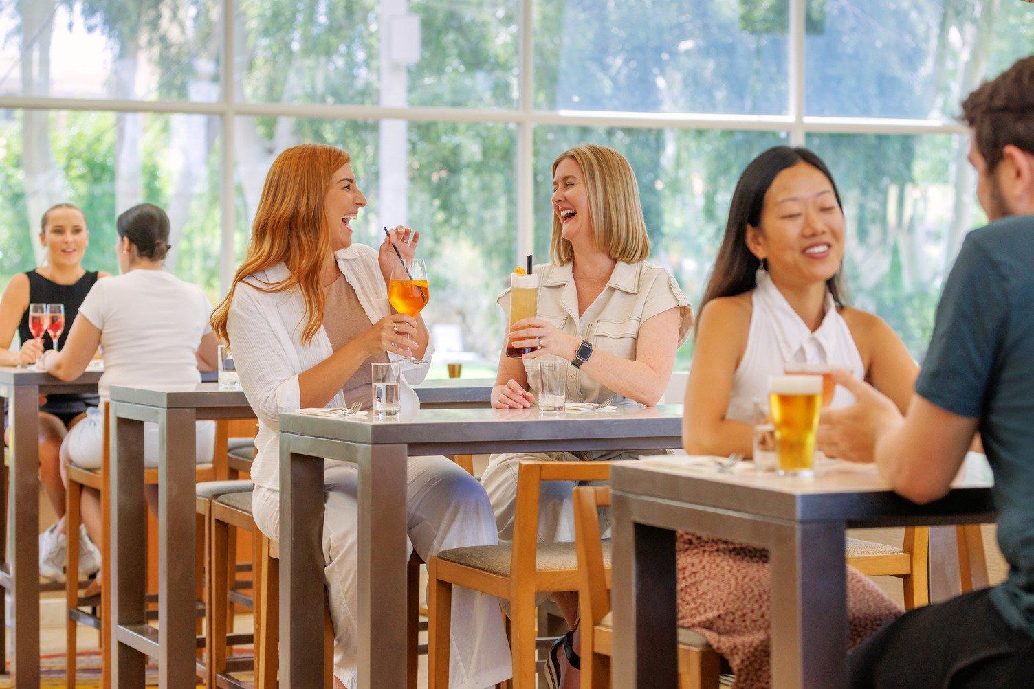 Two ladies laughing together while holding an Aperol spritz and passionfruit cocktail