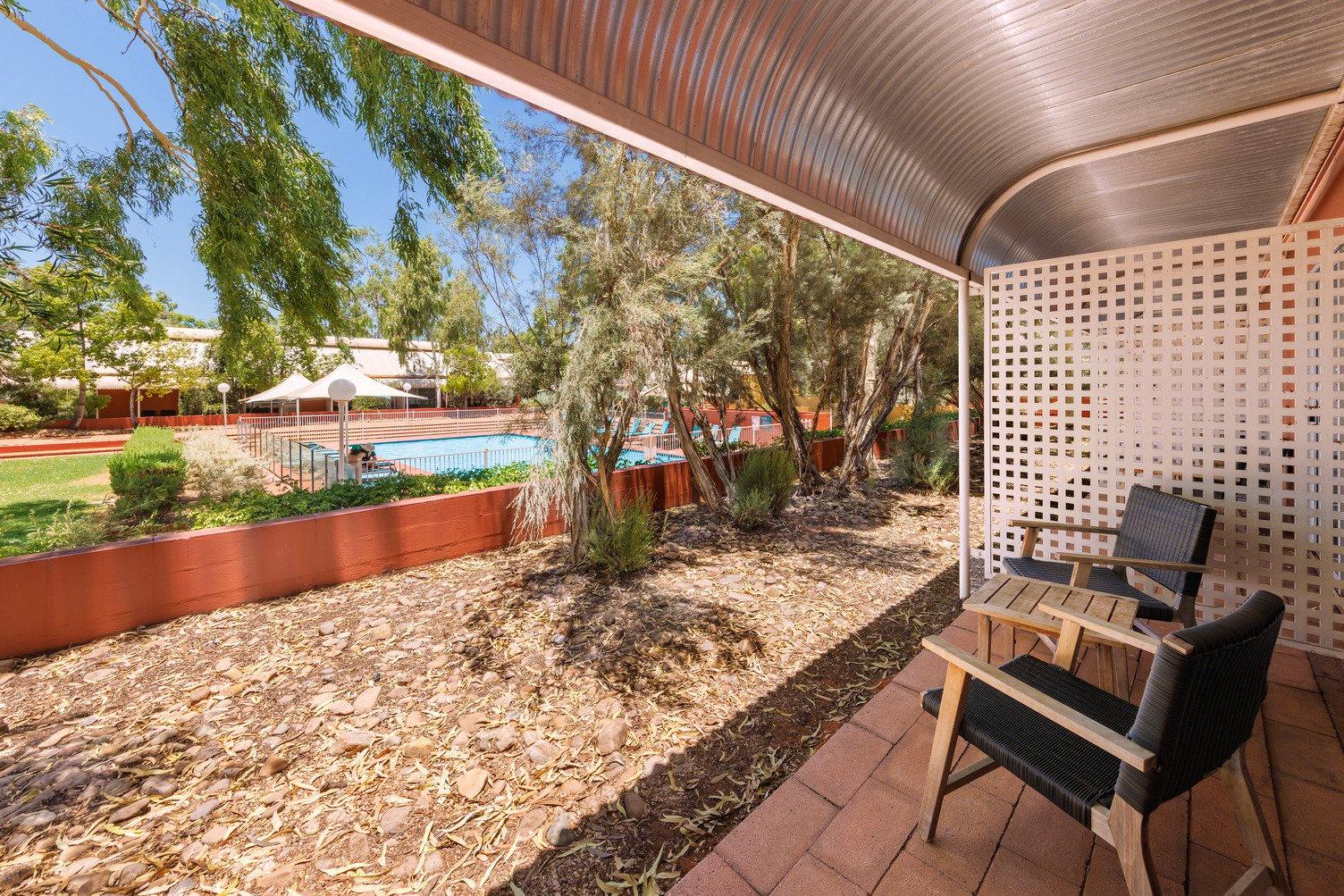 Outdoor area with two chairs and a table looking out towards the Desert Gardens pool with lots of native trees 