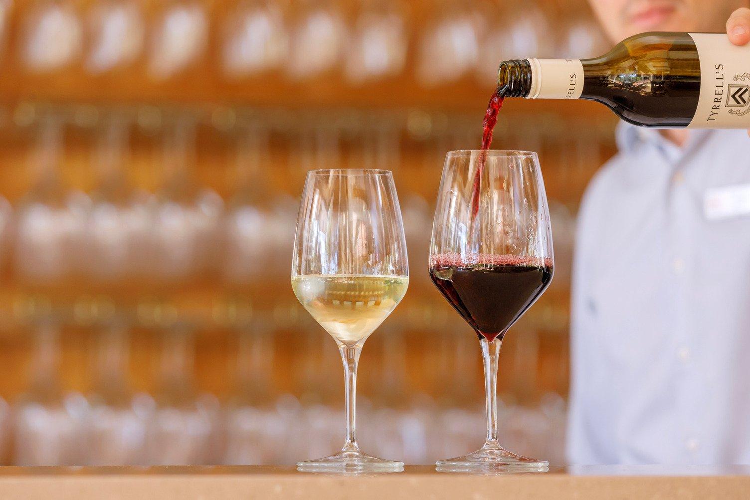 Two glasses of wine. One glass filled half with white wine, and the other glass is currently getting filled with red wine from a bottle
