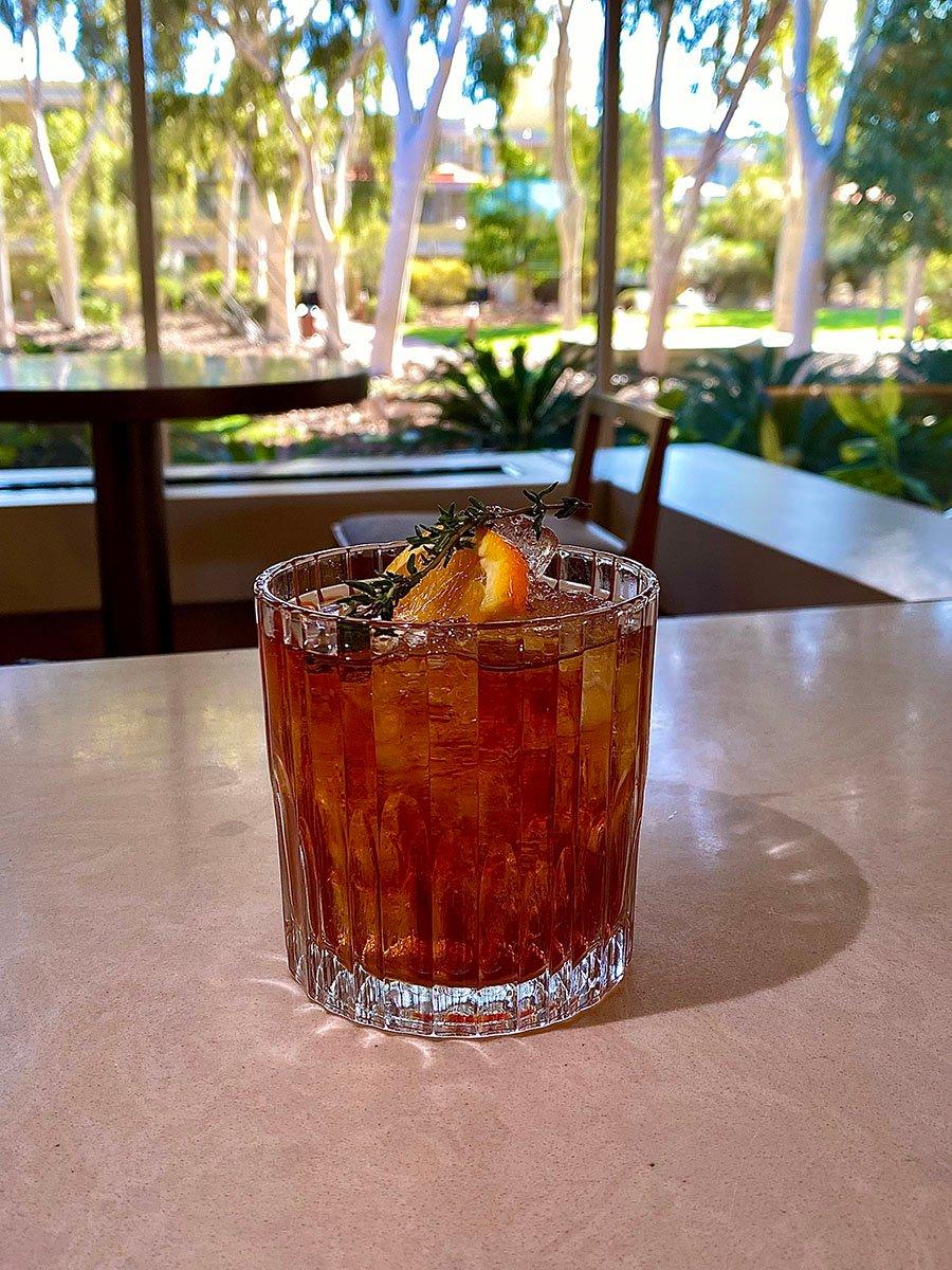 A negroni with native ingrediants served over ice and lemon with Sails in the Desert garden in the backdrop