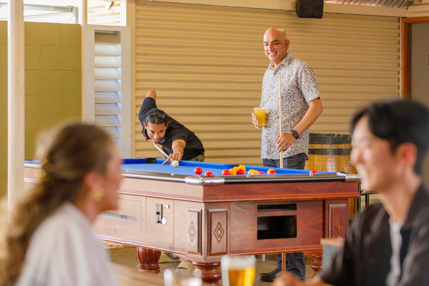 A couple cheersing their drink while two males play pool in the background