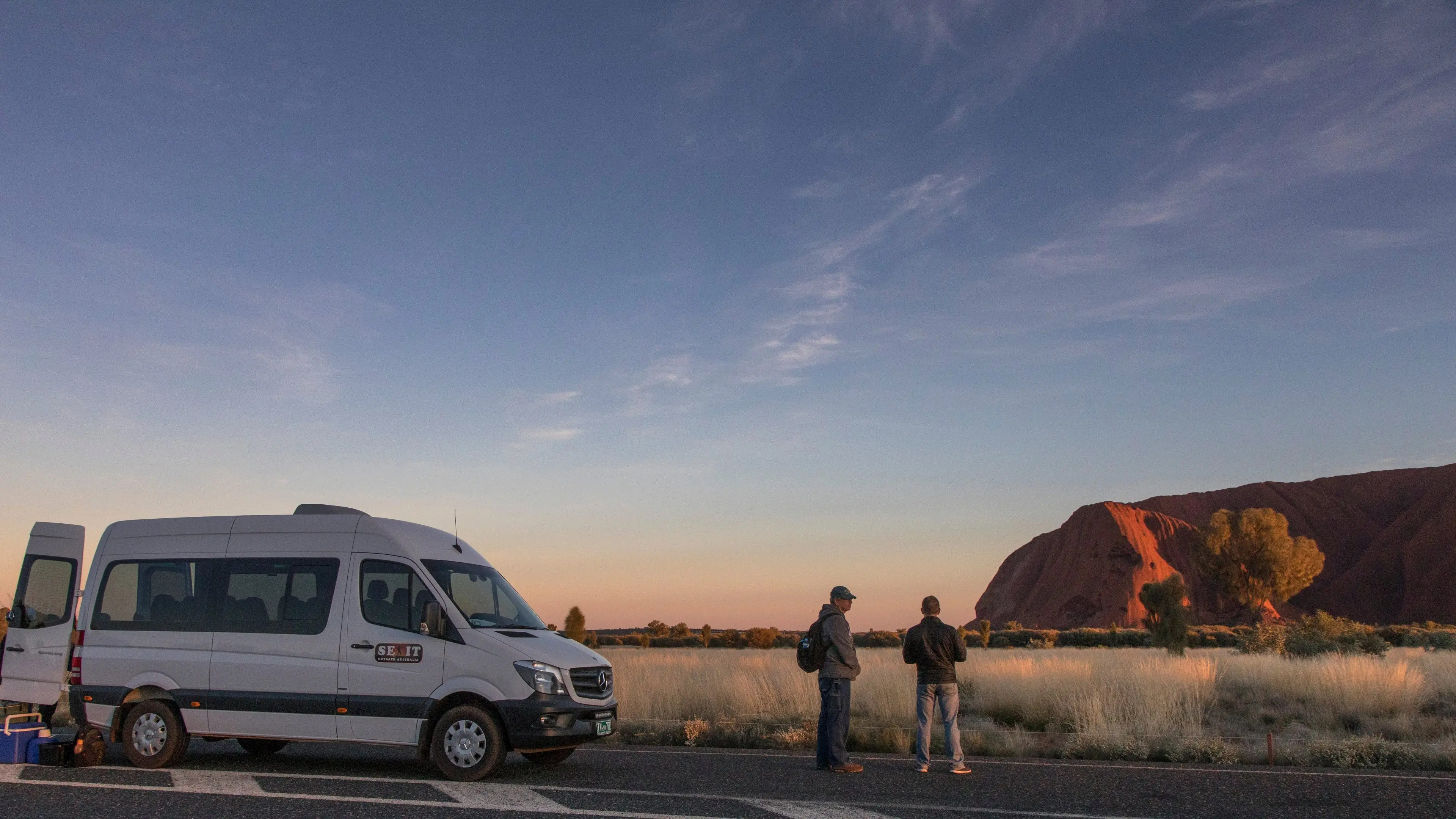 A couple standing beside a van with Ayers Rock in the background