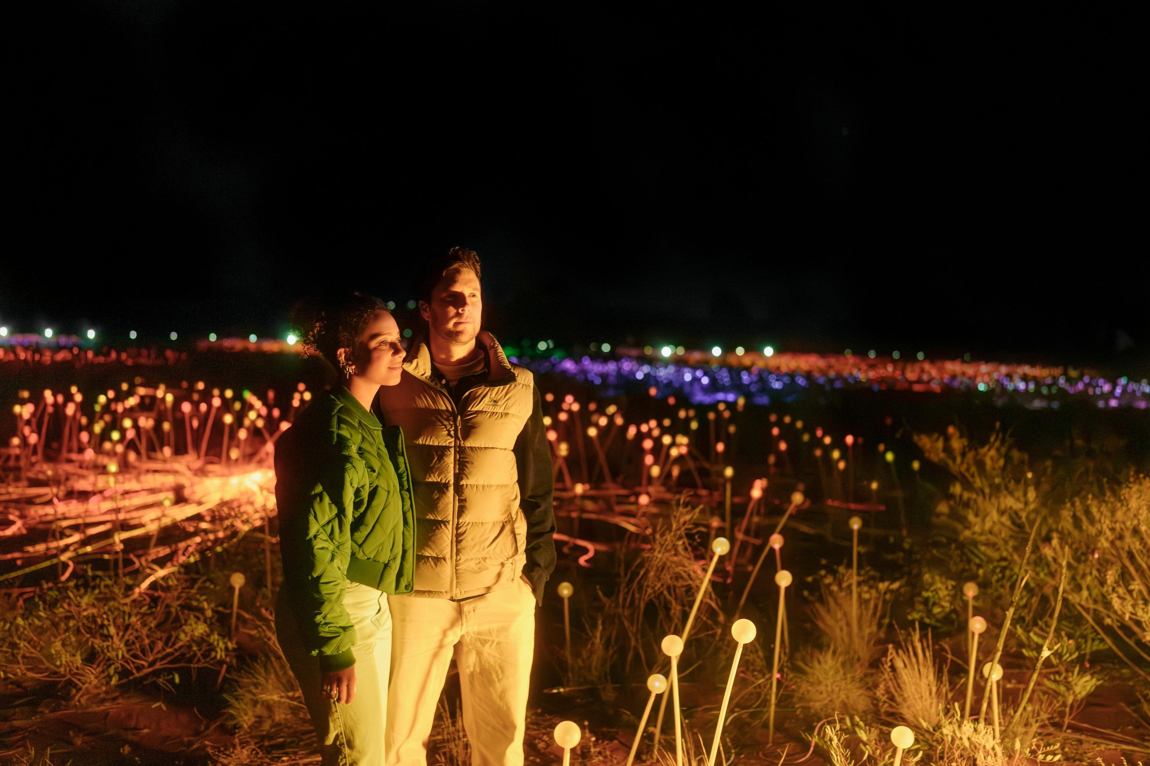 A couple stands arm in arm in an illuminated field at night