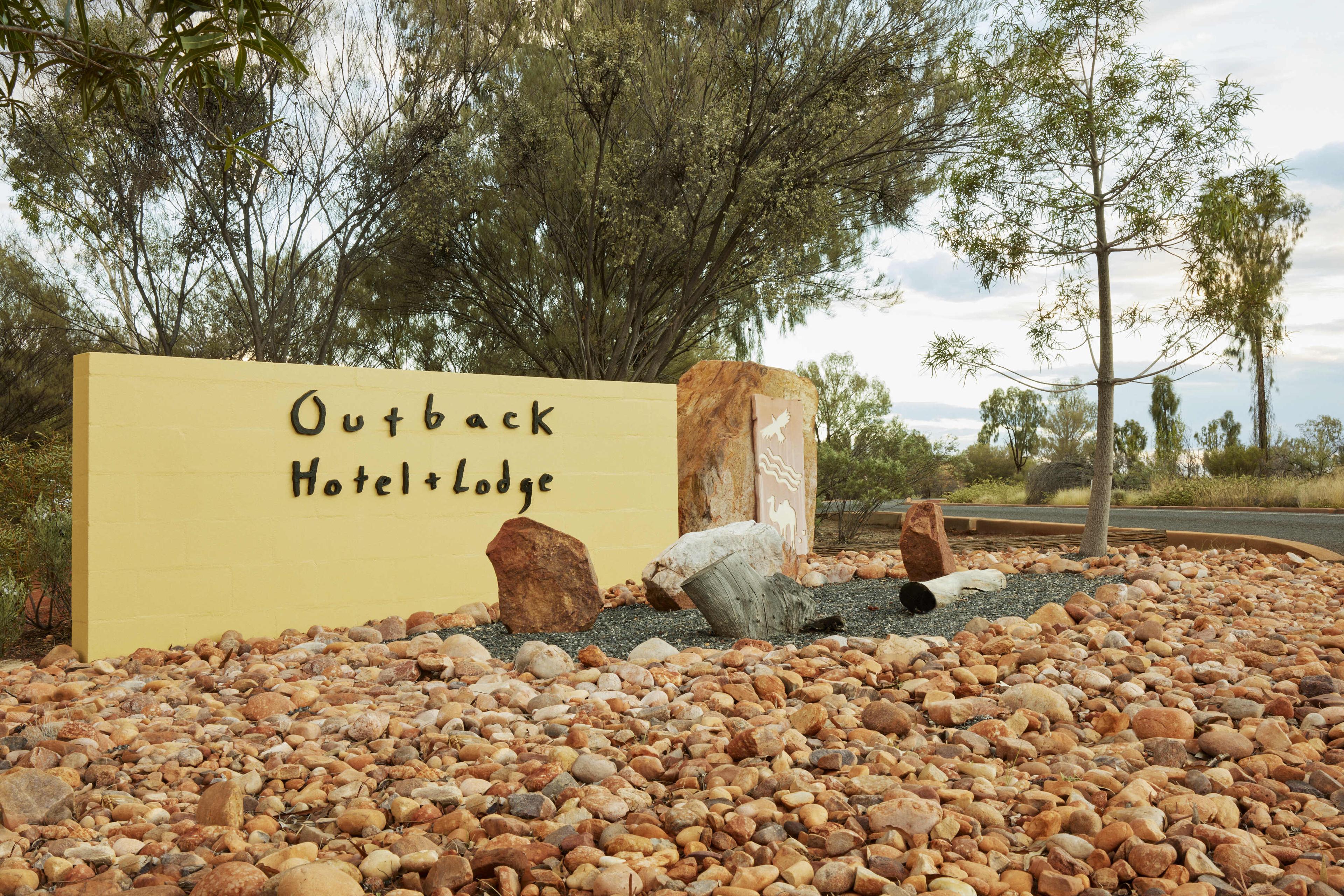A baby yellow sign displaying Outback Hotel + Lodge in front of accommodation with rocks and trees