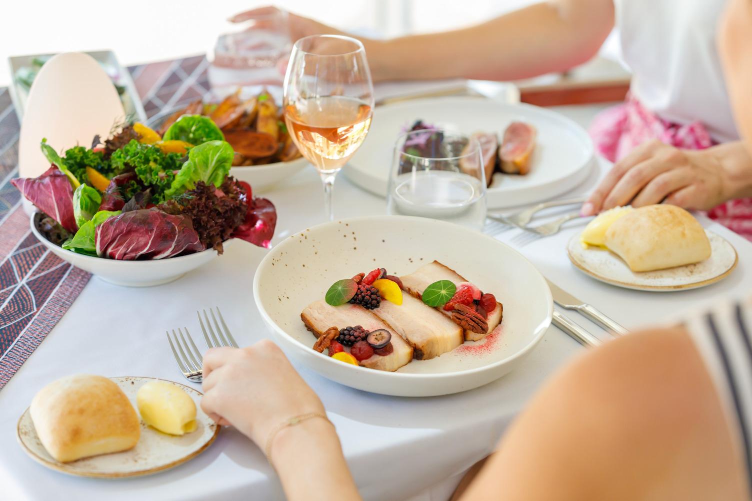 Two people enjoying their meals with a bowl of salad and glass of wine