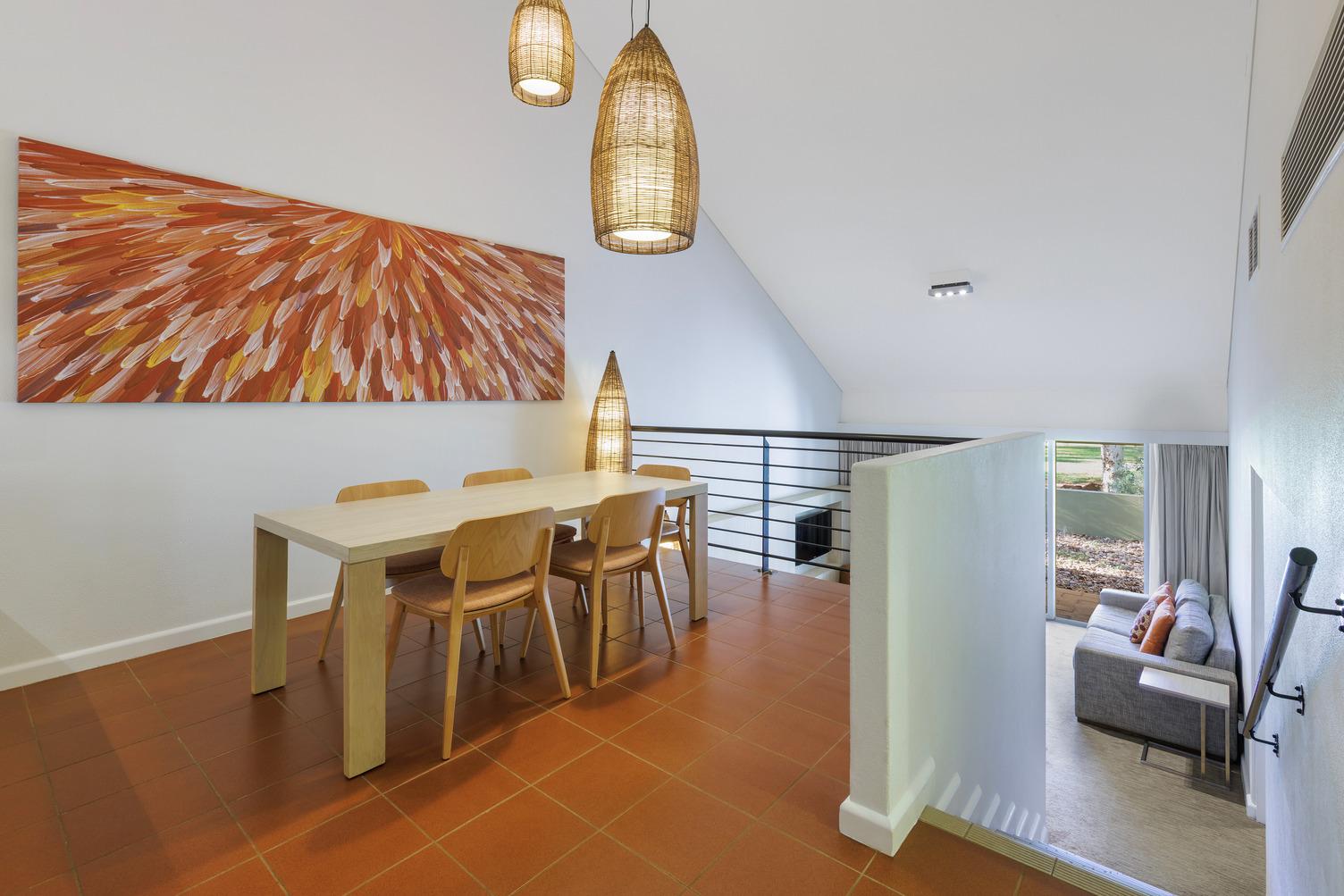Dining area with a table and 4 chairs with a beautiful, large piece of artwork on the wall, downstairs will lead you to the loungeroom with grey couch and courtyard