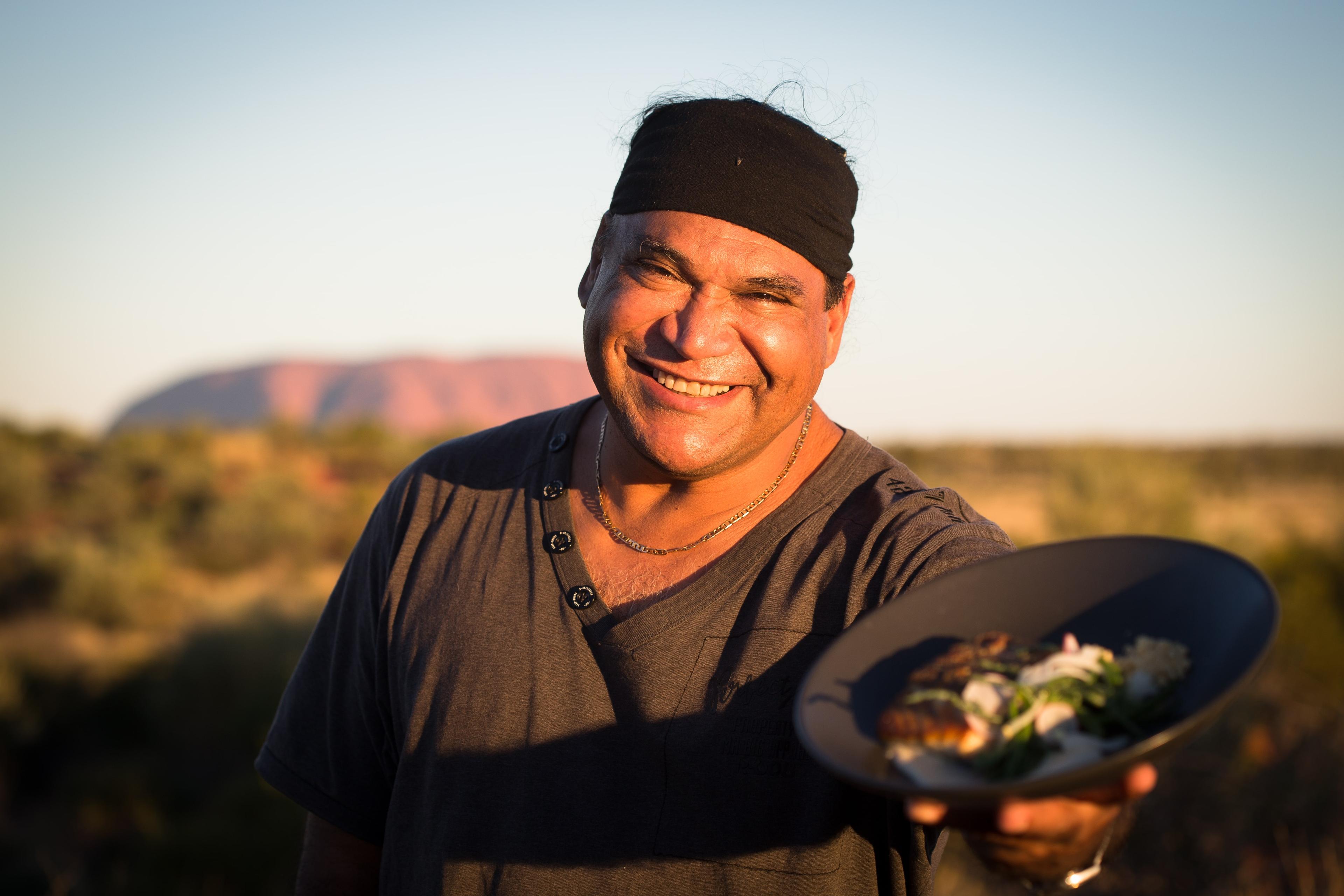 Chef Mark Olive presenting a dish in front of Uluru