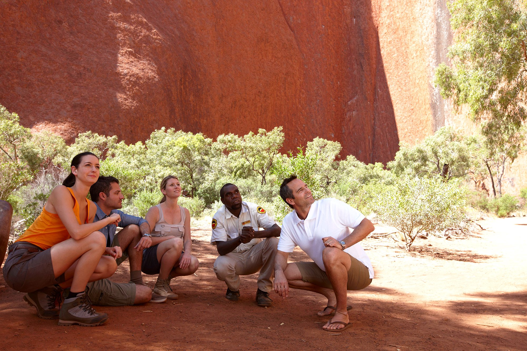 people crouched in the shadows of Ayers Rock
