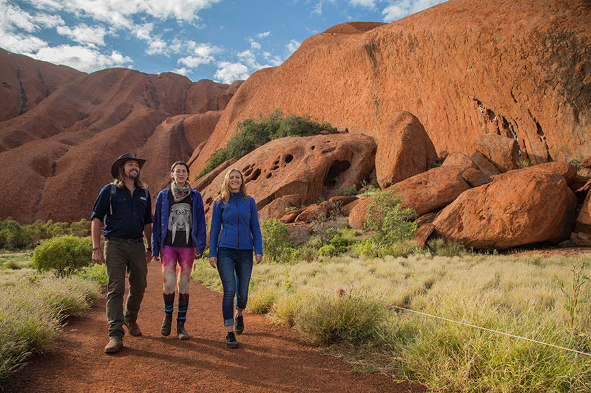 Three people hike on a sunny day near Uluru
