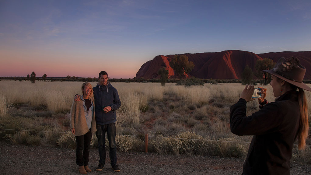 couple having their photo taken with a s unset and Ayers Rock in the background
