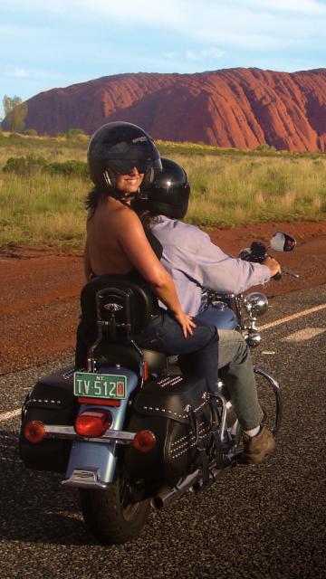 couple riding Harley motorcycle in front of Uluru