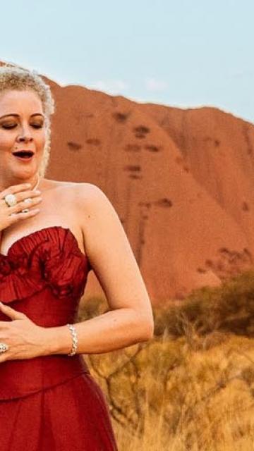 Opera singer in red gown in front of Uluru Ayers Rock
