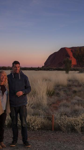 couple having their photo taken with a s unset and Ayers Rock in the background